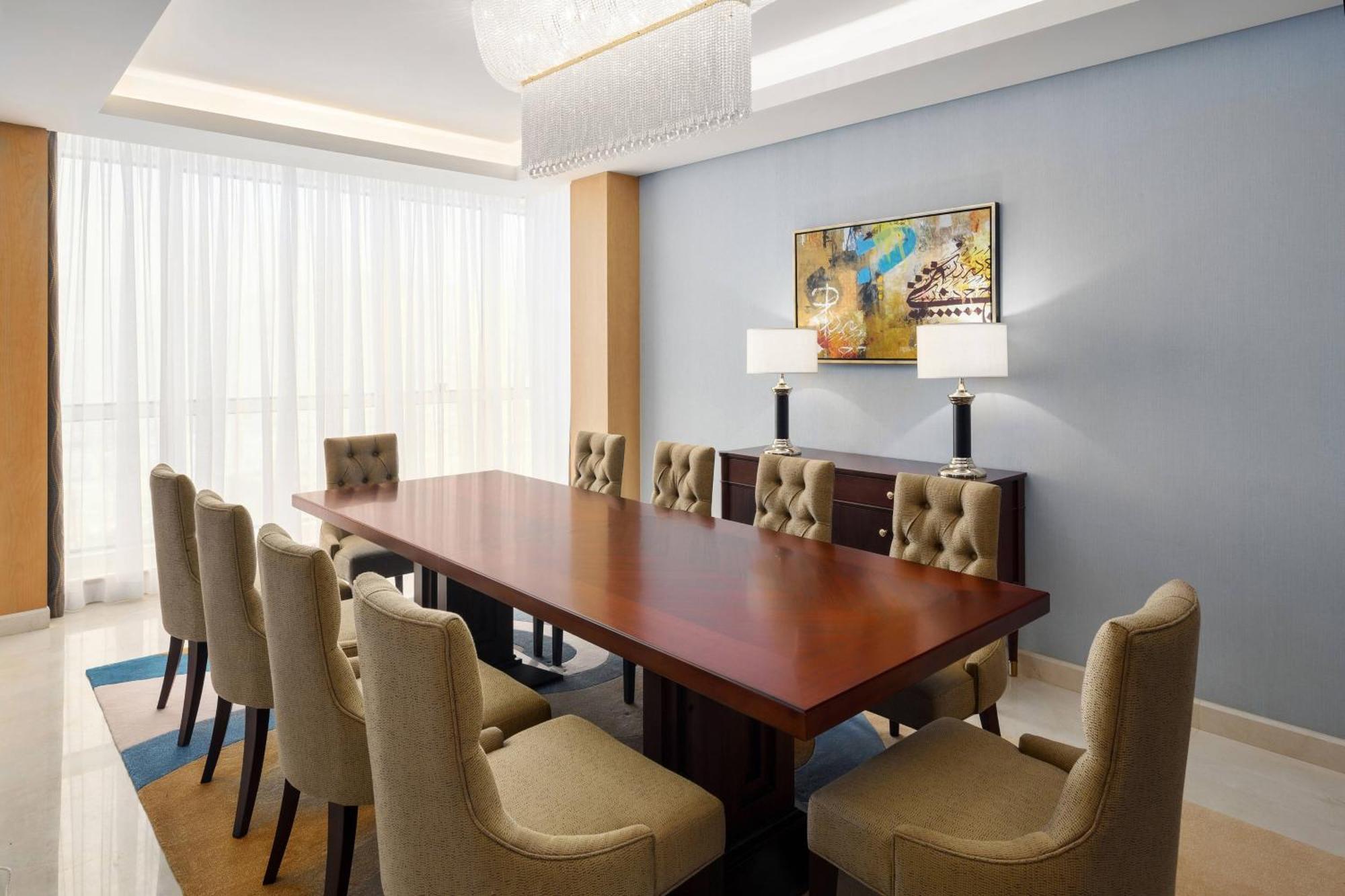 Sheraton Makkah Jabal Al Kaaba Hotel Μέκκα Εξωτερικό φωτογραφία The photo shows a spacious and elegantly designed conference room. It features a large wooden conference table surrounded by upholstered chairs. The chairs have a beige color and a tufted design. On one side of the room, there are two contemporary la