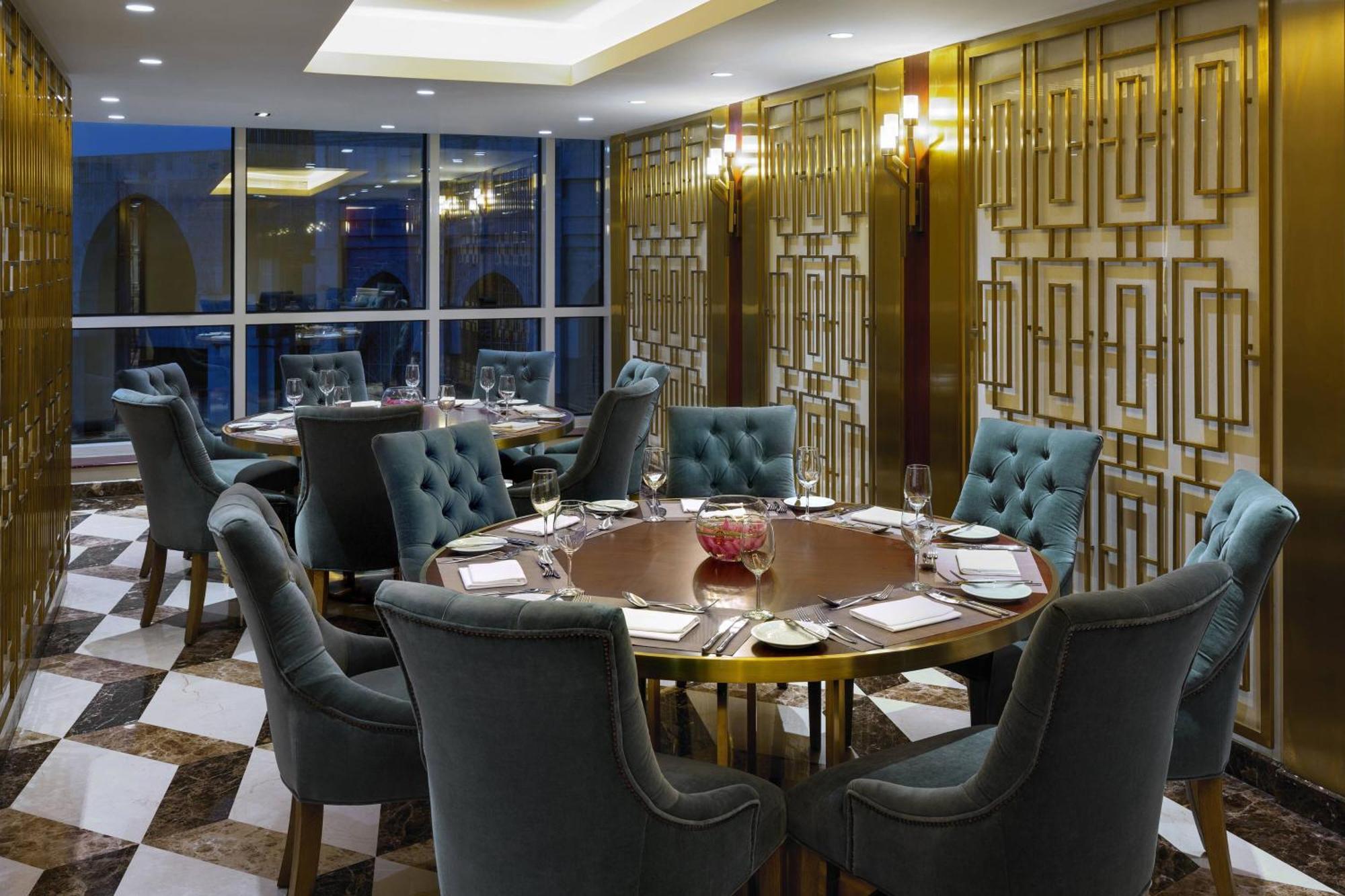 Sheraton Makkah Jabal Al Kaaba Hotel Μέκκα Εξωτερικό φωτογραφία The photo shows an elegant dining room with a sophisticated ambiance. It features a round wooden table at the center, surrounded by plush chairs upholstered in a soft, teal fabric. The room has a stylish décor, highlighted by a geometrically patterne